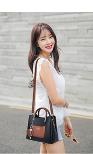 Detail of black pebbled leather tote bag with brown pocket and heart charm accessory