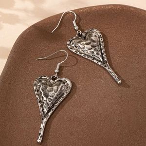 Vintage hammered silver heart drop earrings on a rustic textured brown stone background