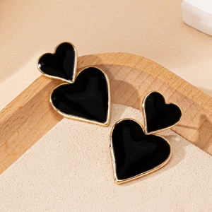 Dettaglio di eleganti orecchini a doppio cuore in smalto nero su vassoio in legno