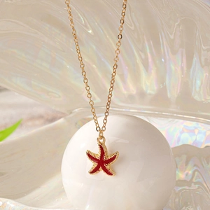 Golden starfish pendant necklace with red enamel finish on an iridescent shell background