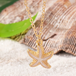 Starfish pendant necklace with pink enamel and gold chain on beach background