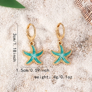 Blue enamel starfish drop earrings with golden base on beach sand and sea shell background
