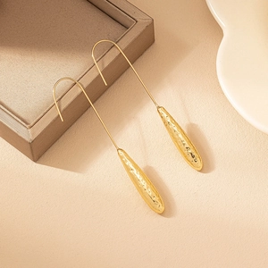 Elegant gold teardrop earrings with hammered texture and long hooks on a warm background