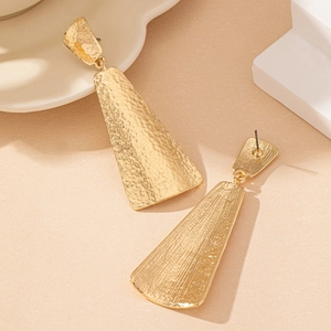 Macro view of gold geometric drop earrings showing textured hammered finish and connectors