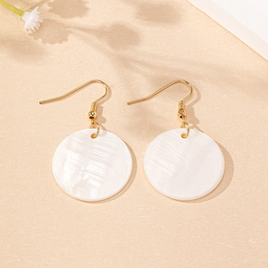 Détail de boucles d'oreilles disque en nacre avec crochets dorés sur fond neutre