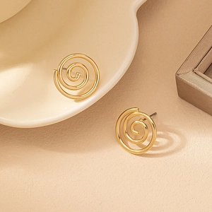 Orecchini a perno a spirale dorati dal design minimale su un piatto di ceramica