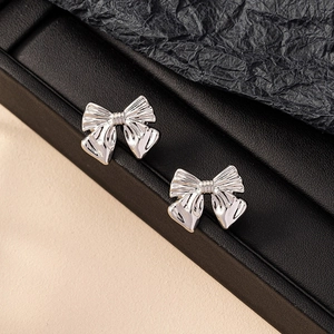 Polished silver bow knot stud earrings for women on a professional black textured display