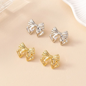 Detail of bow-shaped stud earrings featuring intricate pleated metal texture and metallic luster
