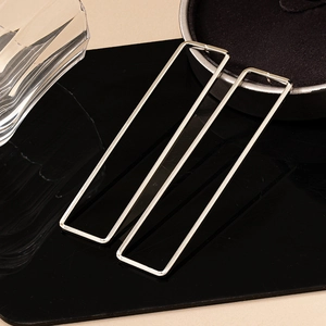Boucles d'oreilles rectangulaires argentées minimalistes sur surface noire réfléchissante