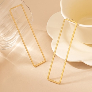 Gros plan détaillé de boucles d'oreilles rectangles évidées dorées sur fond minimaliste