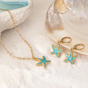 Goldenes Seestern-Schmuckset mit blauer Emaille-Halskette und Creolen auf weißem Sand