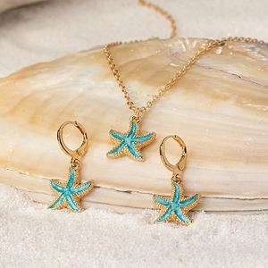 Seestern Halskette und Ohrringe Set in Gold und Türkis auf Sand und Muscheln dekoriert