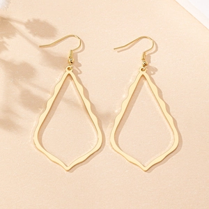 Gros plan de boucles d'oreilles goutte dorées ajourées avec texture ondulée sur papier