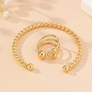 Detail of twisted cable gold cuff bracelet and triple ball open ring on sandy surface