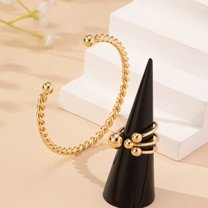 Elegant gold braided twist open bangle and beaded rings set on a minimalist display