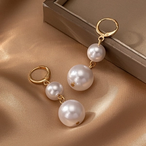 Gros plan de boucles d'oreilles perles dorées posées sur un tissu en soie champagne