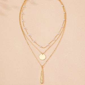 Detail of triple-layer gold necklace featuring pearls, disc and bar pendants
