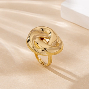 Detail of a golden twisted knot ring on a textured surface with soft lighting