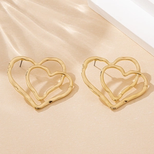 Macro detail of gold double heart earrings featuring an irregular hammered metal texture