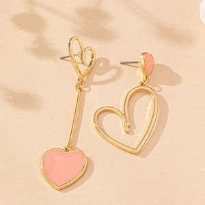 Boucles d'oreilles cœur rose asymétriques dorées sur un fond beige texturé