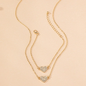 Macro detail of a layered gold necklace featuring two sparkling heart-shaped pendants