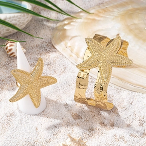 Golden starfish jewelry set with textured open bracelet and ring on a beach background
