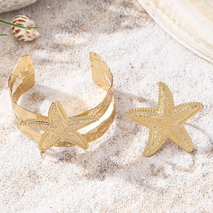 Close-up of golden starfish jewelry set with textured surface on beach sand background