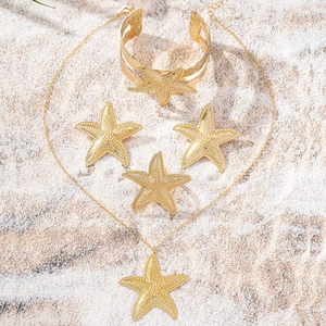 Détail d'un ensemble de bijoux étoile de mer dorés texturés sur fond de sable blanc