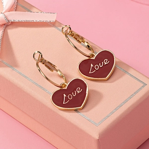 Dettaglio di orecchini a cuore bordeaux con scritta Love su una confezione regalo