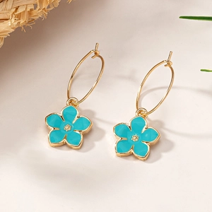 Détail de créoles dorées avec pendentifs fleurs en émail bleu ciel sur fond estival