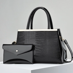 Black crocodile embossed tote bag and clutch set with gold hardware on white pedestal