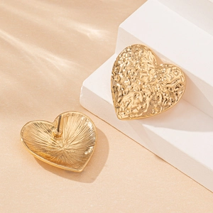 Golden heart-shaped earrings with hammered texture on minimalist geometric stand
