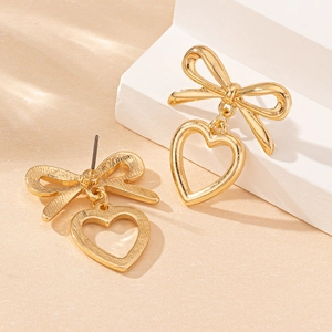 Elegante goldene Schleifenohrringe mit hohlen Herzanhängern auf warmem Hintergrund