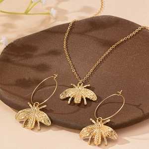 Parure bijoux abeille dorée avec collier et créoles détaillés sur fond beige élégant