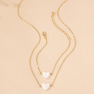 Detail of gold double-layer necklace featuring white shell heart pendants and lobster clasp