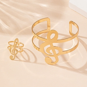 Detailed close-up of gold treble clef cuff bracelet and matching ring set on beige background