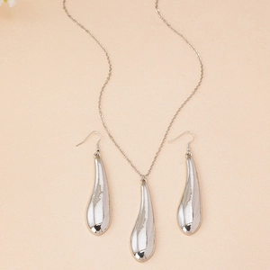 Détails de l'ensemble collier et boucles d'oreilles goutte d'eau argentée sur fond beige
