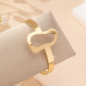 Elegant gold open bangle with abstract hollow heart design on a textured display stand