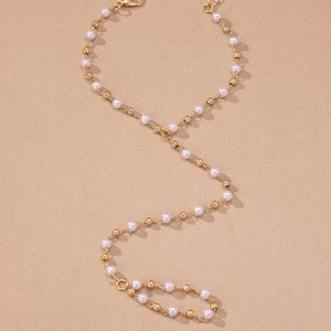 Macro detail of the elegant gold chain body jewelry featuring white faux pearl beads
