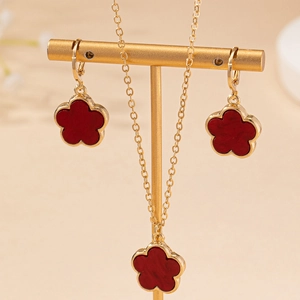 Elegant gold jewelry set with red clover necklace and matching earrings on a display stand
