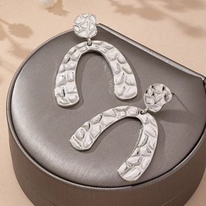Silver hammered metal geometric arch earrings on elegant jewelry box with soft shadows