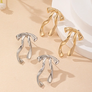 Elegant bow-shaped stud earrings in gold and silver finish on a stone pedestal