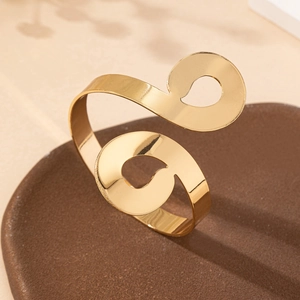 Gold spiral cuff bracelet with geometric teardrop cutouts on polished metal surface