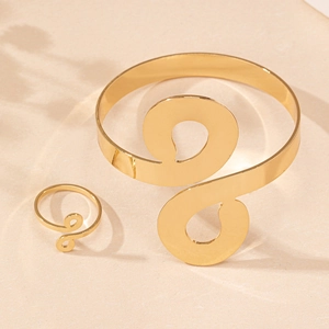 Polished gold infinity spiral arm cuff and matching ring set on a stone surface