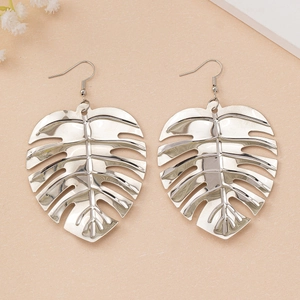 Gros plan de boucles d'oreilles feuilles de monstera argentées au fini poli sur fond rose
