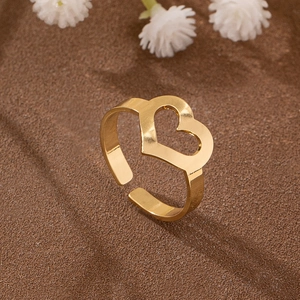Bague dorée ajourée en forme de cœur sur sable avec de petites fleurs blanches