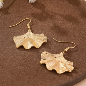 Elegant gold ginkgo leaf dangle earrings with detailed texture on a textured tray