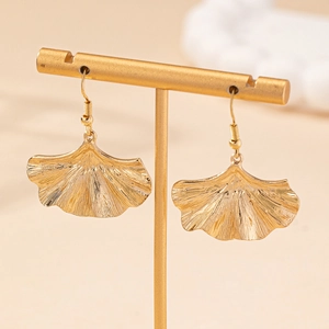 Elegant gold ginkgo leaf dangle earrings with detailed texture on a jewelry display stand
