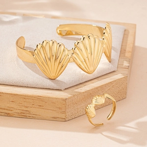 Gold shell relief jewelry set with open ring and bracelet on a wooden stand
