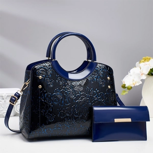 Detail of dark blue glossy patent leather handbag with floral embossed patterns and wallet